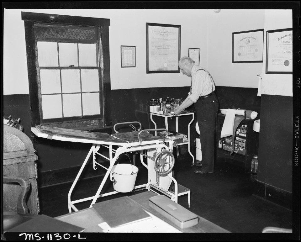 Dr. Anderson, company doctor, in corner of main treatment room in dispensary. He employs other doctors who take care... - NARA - 540682
