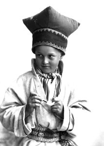 Gutt i samisk drakt, kofte og lue, som renser tobakkspipe - Norsk folkemuseum - NF.25780-870