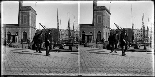 El port de la Barceloneta , amb uns homes en primer terme i més enllà barques , gent i edificis