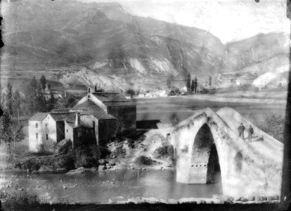 El poble de Fiscal i en primer terme dos homes en un pont sobre el riu Ara