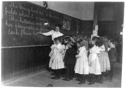 Elementary school children standing and watching teacher write at blackboard, Washington, D.C. LCCN96516051