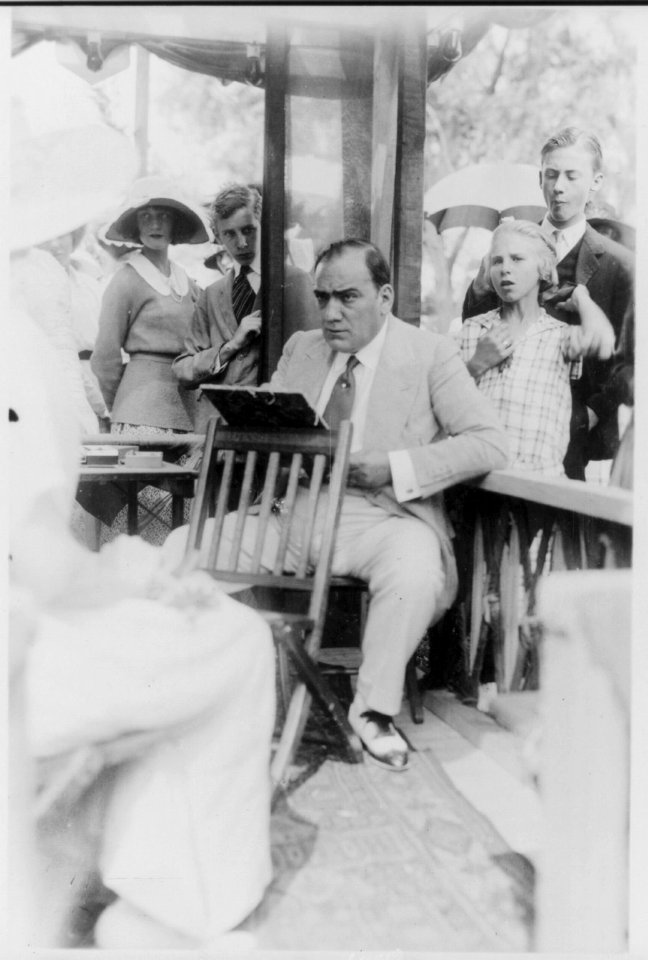 Enrico Caruso, 1873-1921, drawing caricature sketches in booth at charity fair in Southampton, L.I., from right of sitter, onlookers in background LCCN2005680288