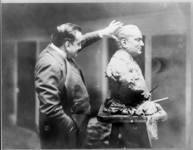 Enrico Caruso, 1873-1921, three-quarter length portrait, standing, right profile, examining a bust sculpture of himself LCCN2005680282