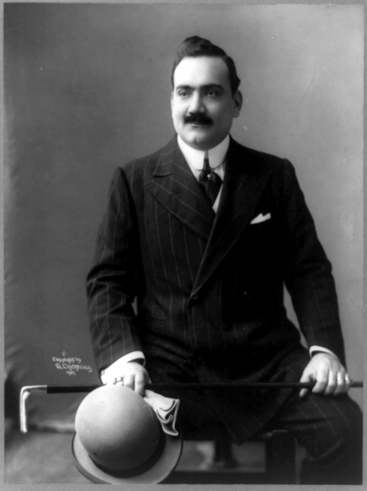 Enrico Caruso, three-quarter length portrait, seated, facing slightly left, holding hat, walking stick, and gloves LCCN89714525