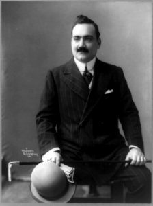 Enrico Caruso, three-quarter length portrait, seated, facing slightly left, holding hat, walking stick, and gloves LCCN89714525