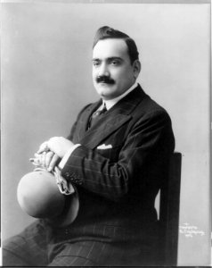 Enrico Caruso, 1873-1921, three-quarter length portrait, seated, facing left, holding hat and gloves LCCN2005680279