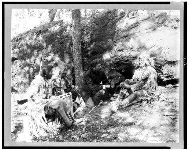 Ernest Thompson Seton, with three Blackfeet Indians, demonstrating how to start a fire using a bow and a stick, rocks and trees in background LCCN93503635
