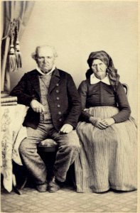 Ett äldre par poserar för fotografen sittande intill ett bord där böcker ligger i trave. Kristianstad - Nordiska Museet - NMA.0039725