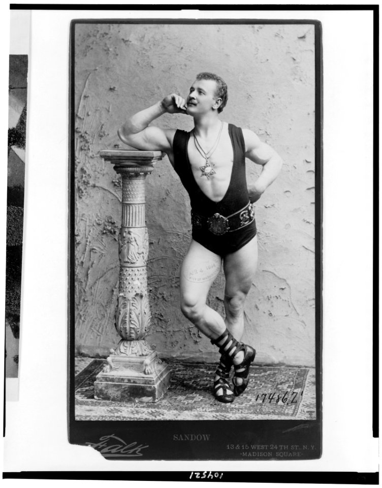 Eugene Sandow, full-length portrait, standing, leaning on column, facing left, wearing wrestling leotard, Roman sandles, and six pointed star pendant LCCN91480334