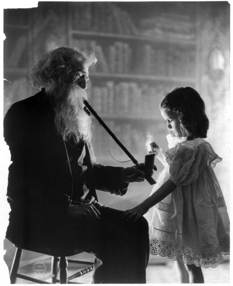 Girl lighting long pipe of old bearded man LCCN2003675175