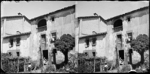 Façana d'una casa amb infants a la porta i un pou al pati