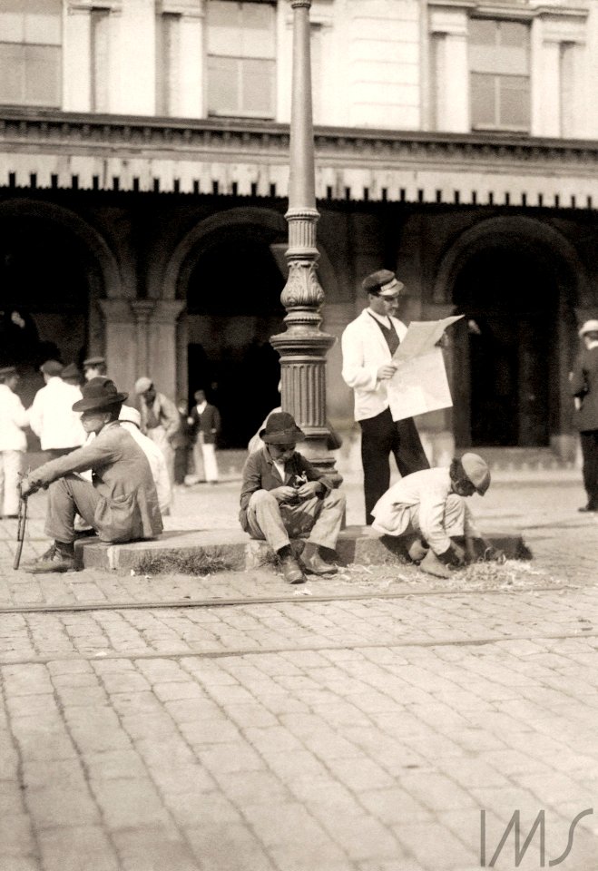 Ferroviário lê jornal, cercado por carregadores de malas, em frente à Estação da Luz - Vincenzo Pastore