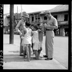 Filipino children make friends with two Naval officers in downtown Manila, hoping for a gift in return. - NARA - 520951