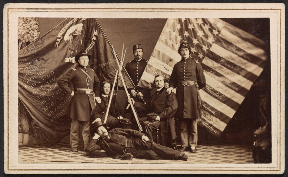 Five unidentified soldiers of the 63rd New York Infantry Regiment in uniform and one unidentified man in civilian dress with federal and state battle flags and rifle stack) - S.J. Thompson & LCCN2013645645