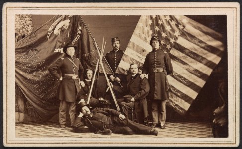 Five unidentified soldiers of the 63rd New York Infantry Regiment in uniform and one unidentified man in civilian dress with federal and state battle flags and rifle stack) - S.J. Thompson & LCCN2013645645