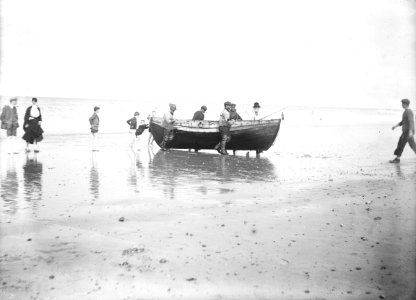 Five fishermen carrying a Sheringham crab boat up the beach, assisted by three boys. RMG P27502