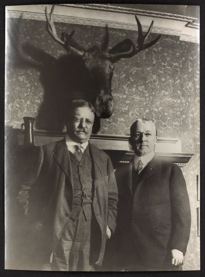 Flashlight taken of Col. Roosevelt and Professor Goode of the Chicago University, in front of a mounted moose head over Professor Goode's fireplace Roosevelt was then campaigning for the LCCN2009631492