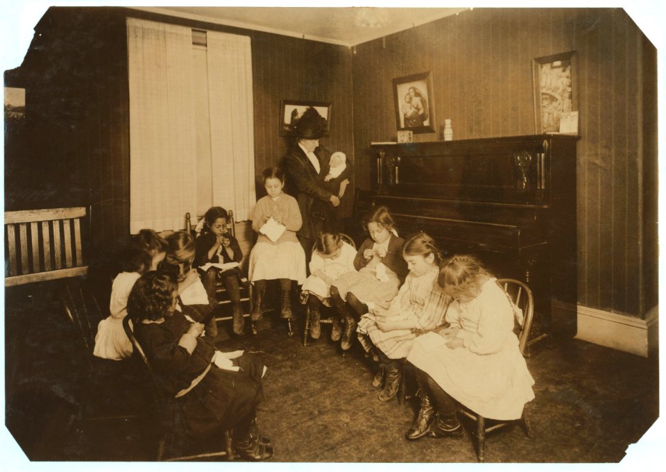 For Child Welfare Exhibit 1912-13.) Sewing class in Sprague House Settlement Providence, R.I. The Director is holding a newly-arrived deserted baby LOC cph.3b06722