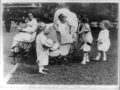 Four small children playing with baby carriages in Washington, D.C., park - African American nursemaid sitting on bench with baby LCCN2001706156