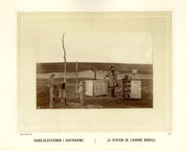 Fra Nordlysstasjonen i Kautokeino. Mann i samedrakt står ute blant kasser med måleinstrumenter - Norsk folkemuseum - NF.15006-033