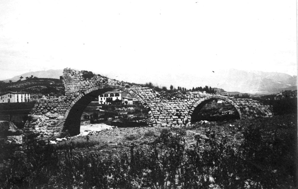 Fragment d'un pont en ruines i cases al fons