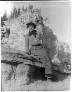 Frances Benjamin Johnston, full-length portrait, sitting on ledge with mountains in background LCCN97513658