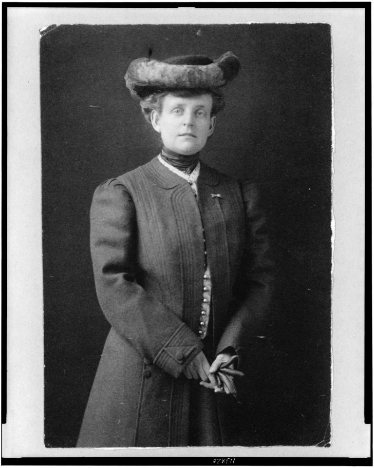 Frances Benjamin Johnston, half-length portrait, standing, facing front, wearing hat and holding gloves LCCN95506164