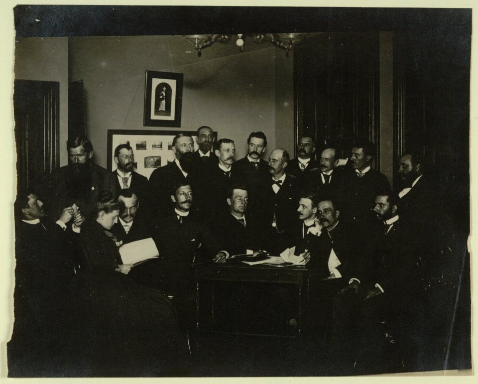 Frances Benjamin Johnston, seated in profile at left, group portrait with 18 unidentified men LCCN2001697160
