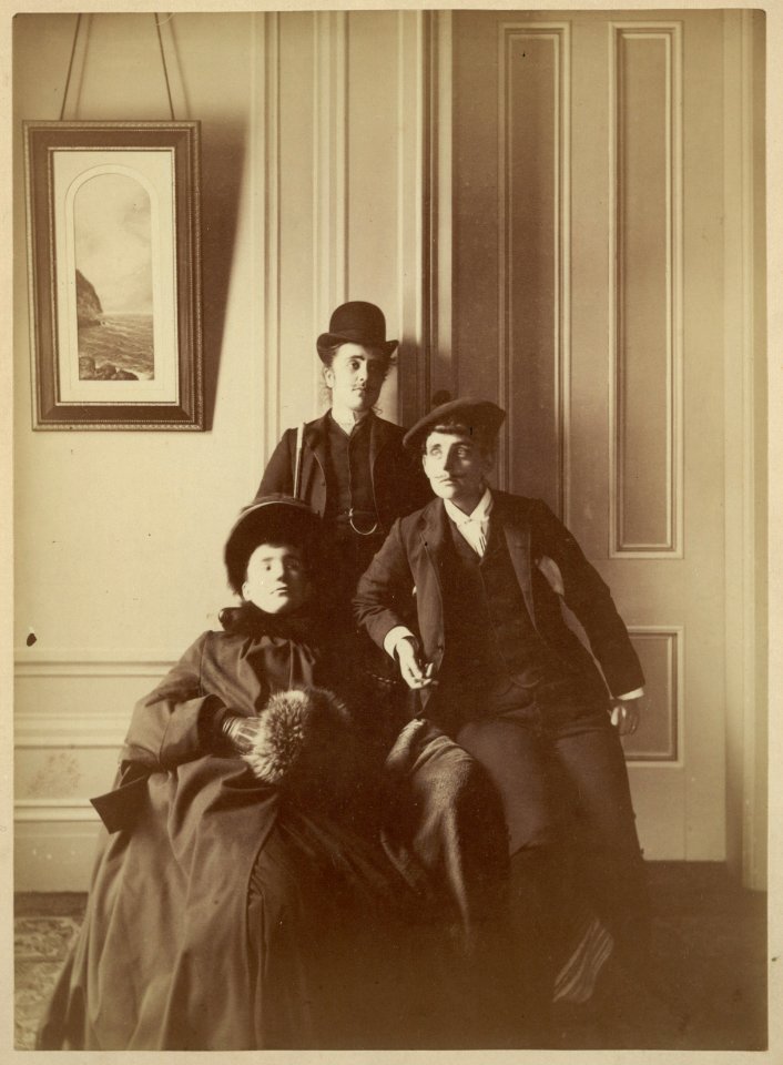Frances Benjamin Johnston (right), full-length self-portrait dressed as a man with false moustache, posed with two unidentified women, one of whom is also dressed as a man LCCN2001697167