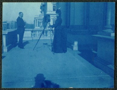 Frances Benjamin Johnston on a balcony of the State, War and Navy Building with a tripod-mounted camera, photographing an unidentified man LCCN2001697168