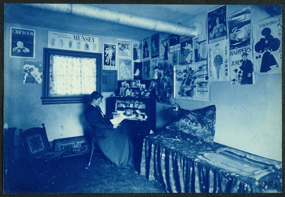 Frances Benjamin Johnston seated at a desk in her studio-office, with adverstising posters on the walls, including the Chap Book, Harper's, and Lippincott's magazines LCCN2001697169