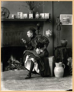 Frances Benjamin Johnston, full-length portrait, seated in front of fireplace, facing left, holding cigarette in one hand and a beer stein in the other, in her Washington, D.C. studio LCCN98502934 photo