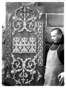 Franciscan monk standing by an intricately decorated wooden panel at Mission Santa Barbara, California, ca.1901-1908 (CHS-4067)