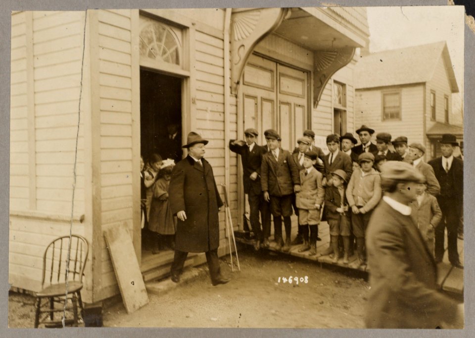 Group of children watching Theodore Roosevelt as he exits a building LCCN2013651225