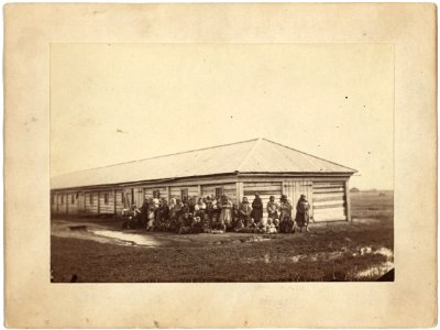 Group of female exiles and their children standing in front of log barracks LCCN99615466