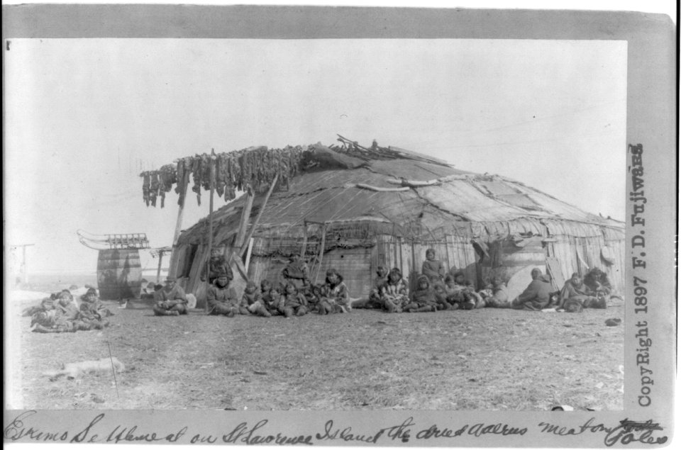 Group of Eskimos outside large circular house on St. Lawrence Island; walrus meat drying on poles LCCN2005691770