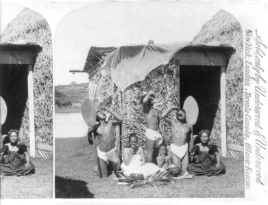 Group of natives eating poi, Hawaiian Islands (in front of grass hut)