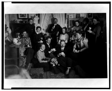Group portrait of friends at social gathering, seated and standing with tea cups, in domestic setting LCCN2001695468