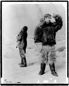 Frederick Albert Cook, full-length portrait, standing, facing right, wearing fur clothing, in front of arctic backdrop, with another man standing behind him LCCN97517569