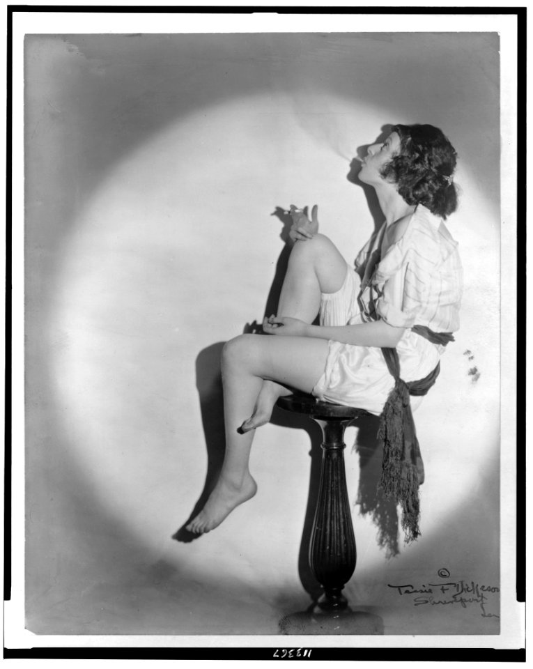 Full length portrait of young woman smoking a cigarette, seated on pedestal, in profile LCCN95504332