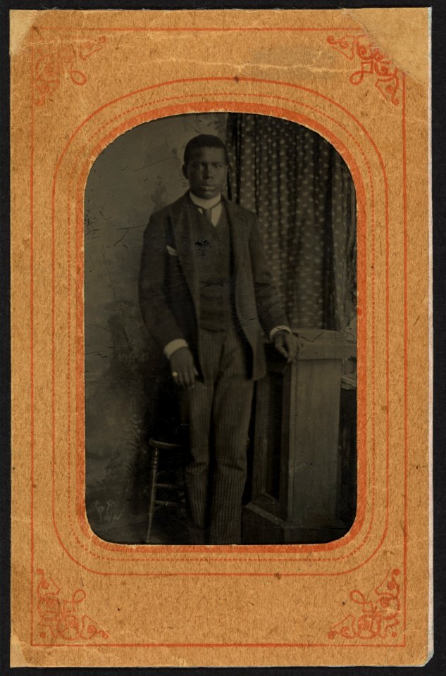 Full-length portrait of a young African American man, standing next to a stool LCCN2010645202