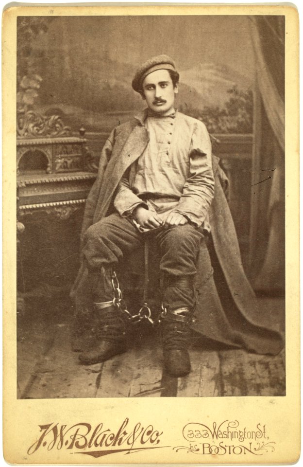 Full-length portrait of a man in convict clothing and leg irons, seated, facing front LCCN99615663