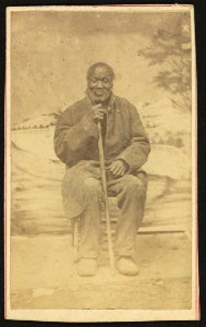 Full-length portrait of an elderly African American man seated with a cane, facing front LCCN2010647828