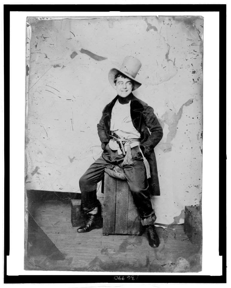 Full-length portrait of a man, dress in frock coat and top hat with sash and pistol at his waist, seated on a crate LCCN2006689590