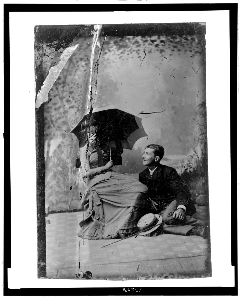 Full-length portrait of a man and a woman. The woman is seated in a chair, the man seated on the floor LCCN2006689635