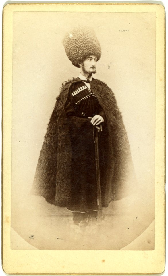 Full-length portrait of a man in cape and sheep skin hat, holding a rifle, facing right LCCN99615610