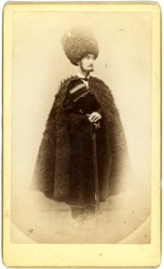 Full-length portrait of a man in cape and sheep skin hat, holding a rifle, facing right LCCN99615610