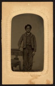Full-length portrait of an African American boy standing beside a chair LCCN2010650824