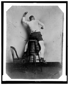 Full-length rear view of a man seated on a barrel, gesturing as if riding a horse LCCN2006689587