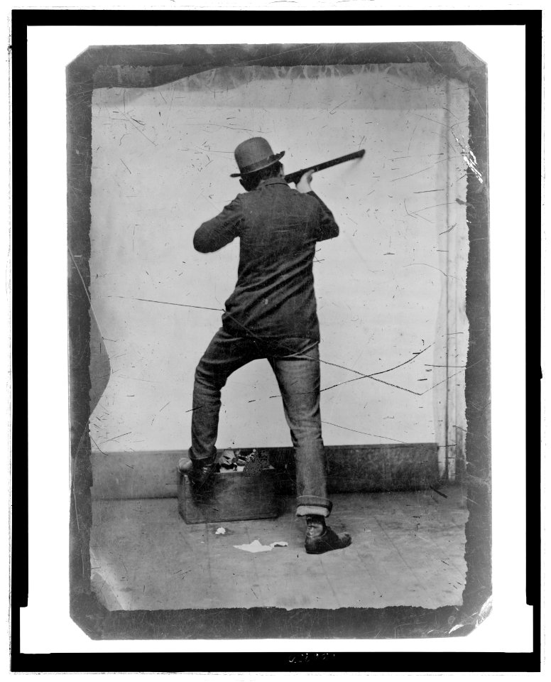Full-length rear view of a man posed as if shooting a rifle LCCN2006689571